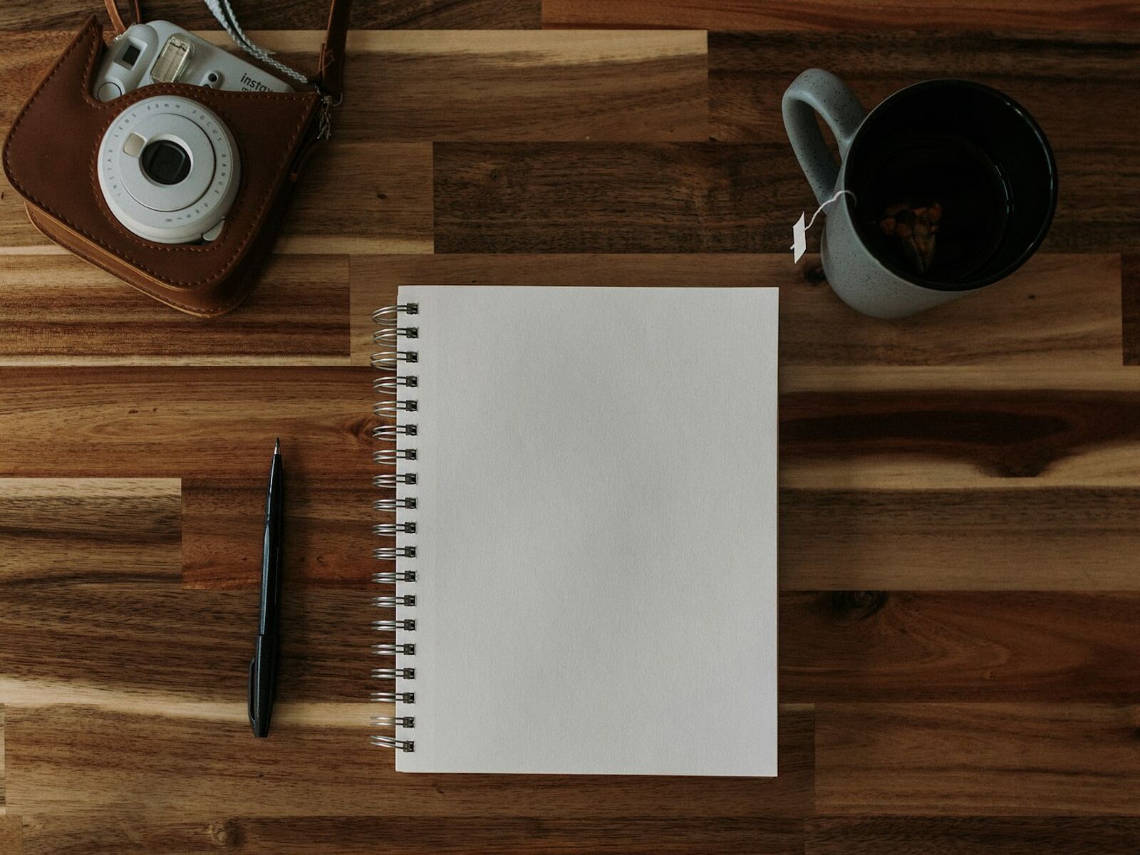 Kamera, aufgeschlagenes Notizbuch, Stift und eine Tasse Kaffee auf einem Holztisch